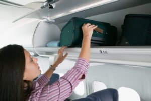 Woman Stowing Baggage on Airplane --- Image by © ColorBlind Images/Blend Images/Corbis